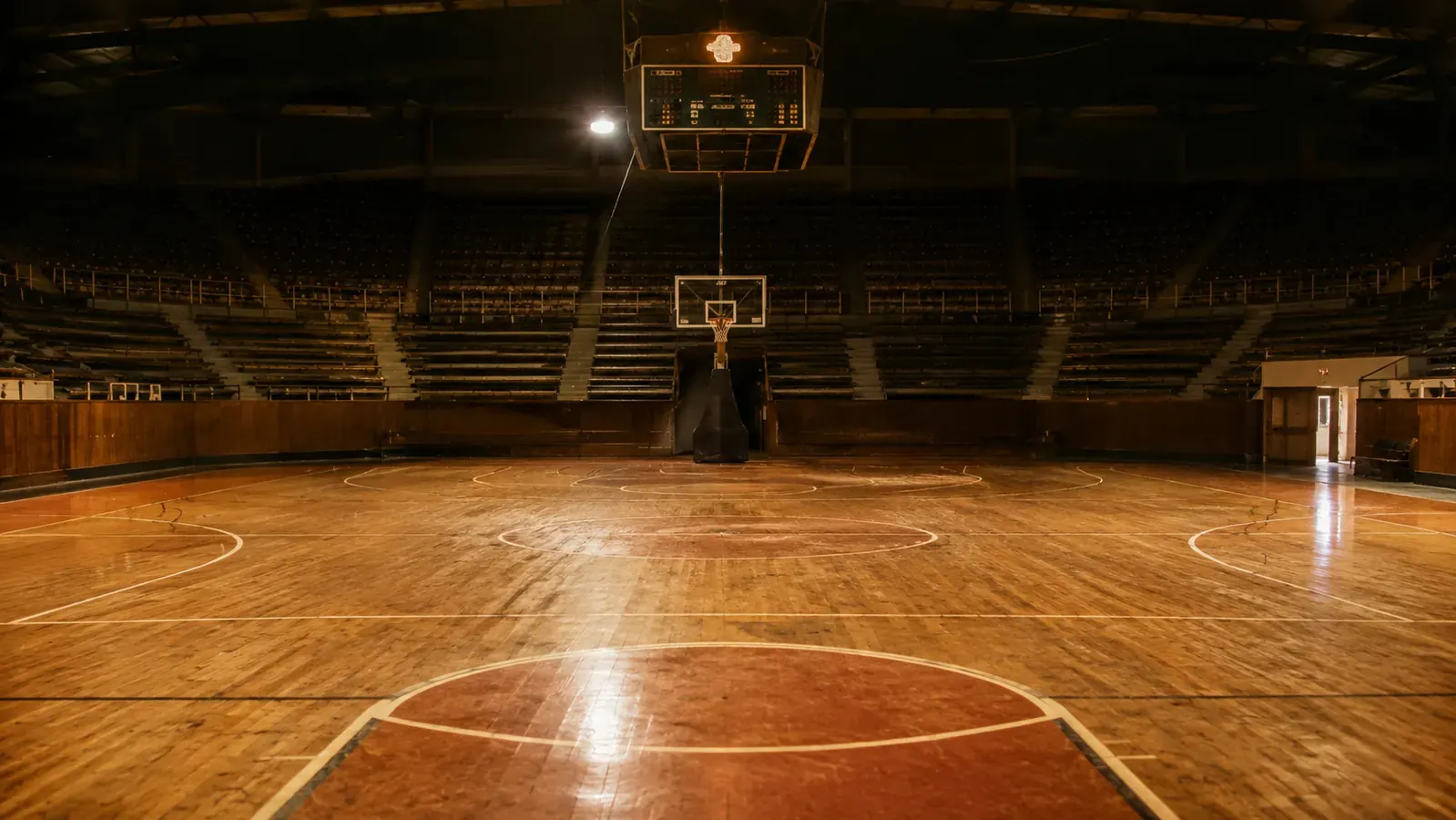 An old hardwood basketball court from the late 1980s with a scoreboard overhead and a packed arena in soft focus